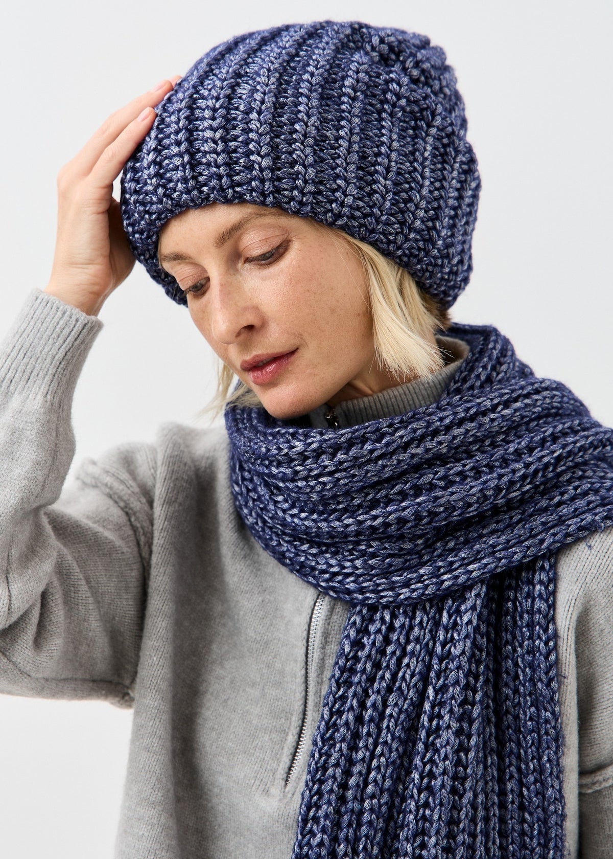 BRIKOLY Lustre Denim Melange oversized knit beanie worn by a model looking down with a matching scarf.