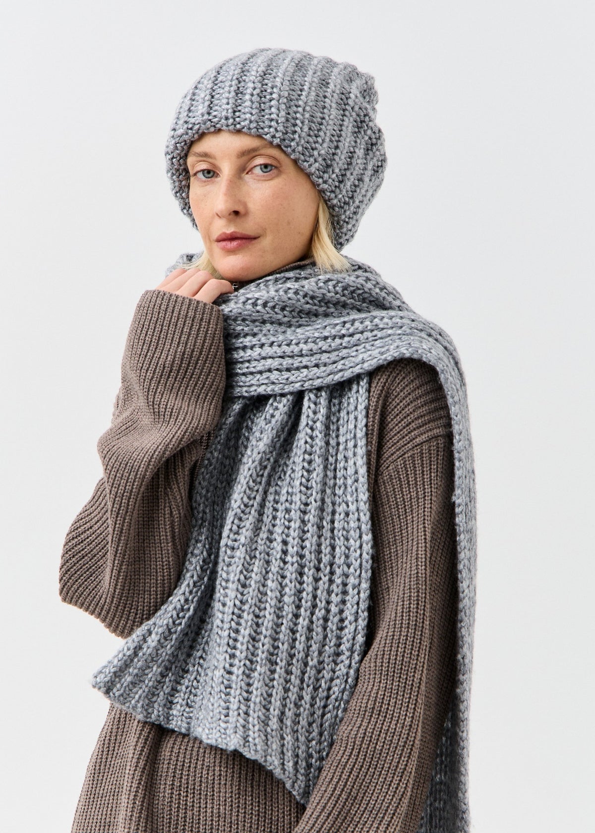 BRIKOLY Lustre Gray Melange knit scarf worn by a model touching the scarf near the chin.
