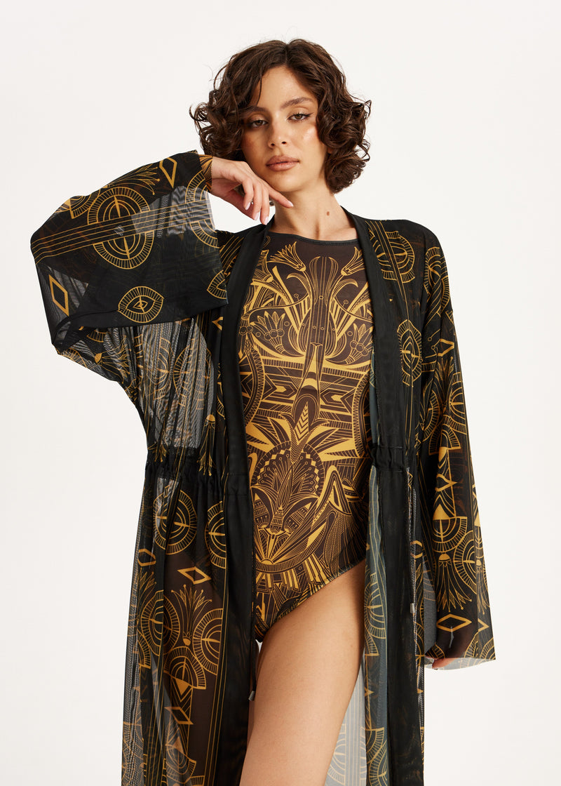 Woman wearing a black and gold patterned swimsuit with a matching cover-up on a white background