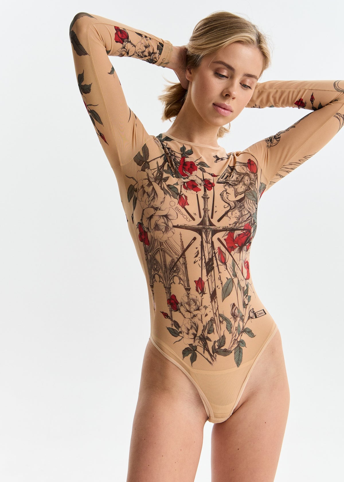 Model wearing a beige bodysuit with intricate black and red floral and cross design on a white background