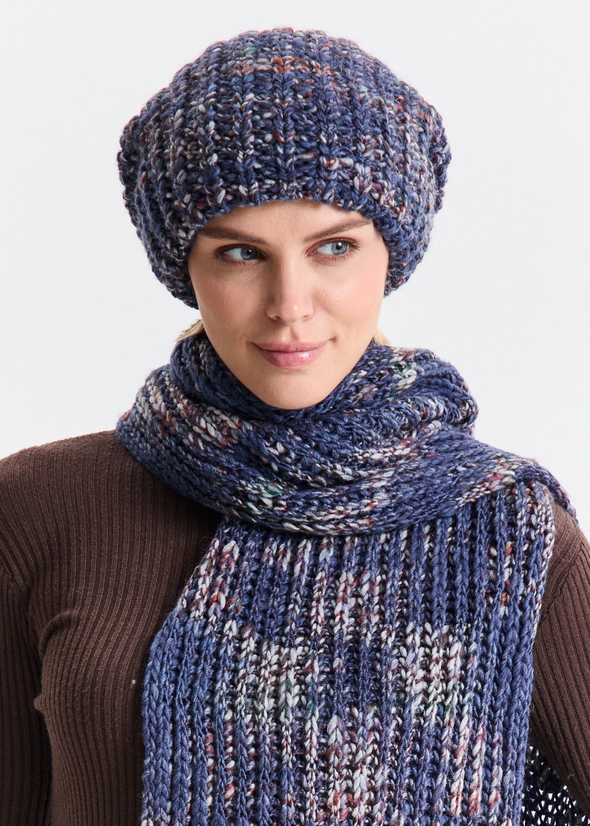 Woman wearing a blue knitted hat and scarf against a white background