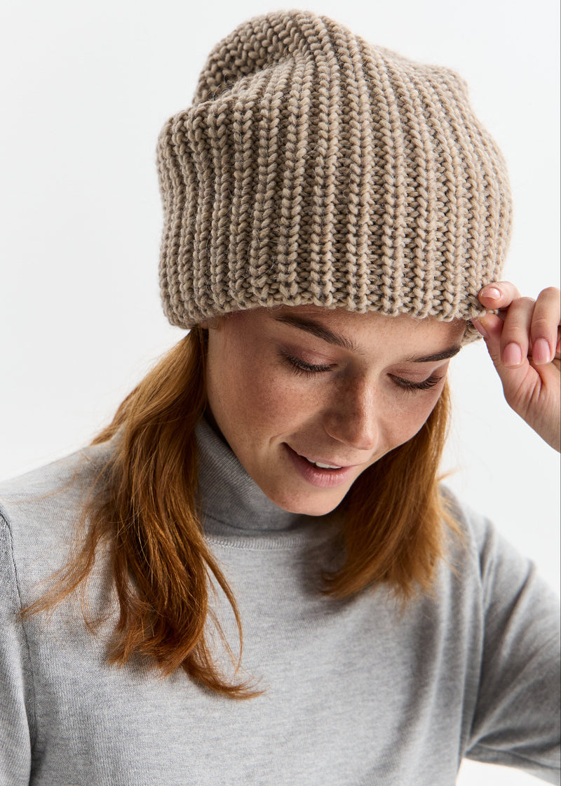 Person wearing a beige knitted beanie on a plain background