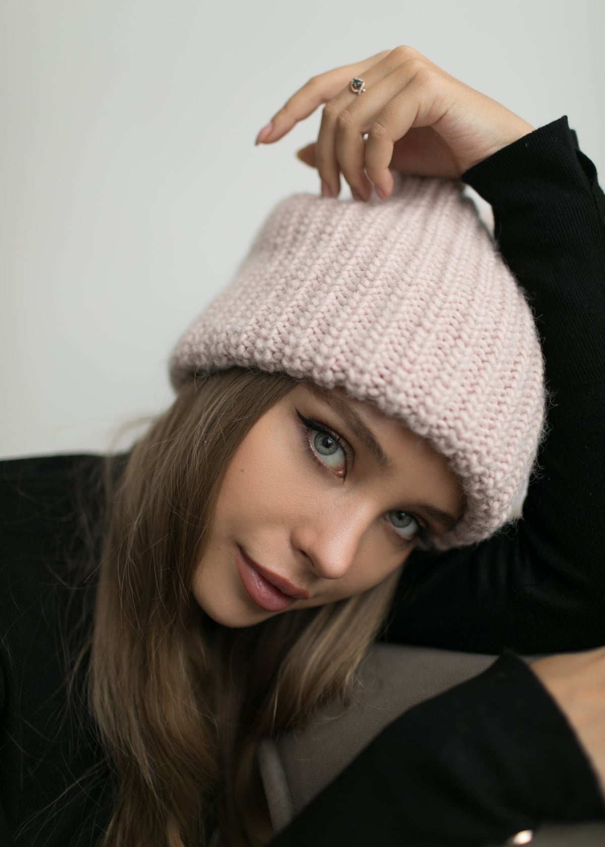 BRIKOLY London Pink knit beanie shown on a model leaning forward and holding the crown.