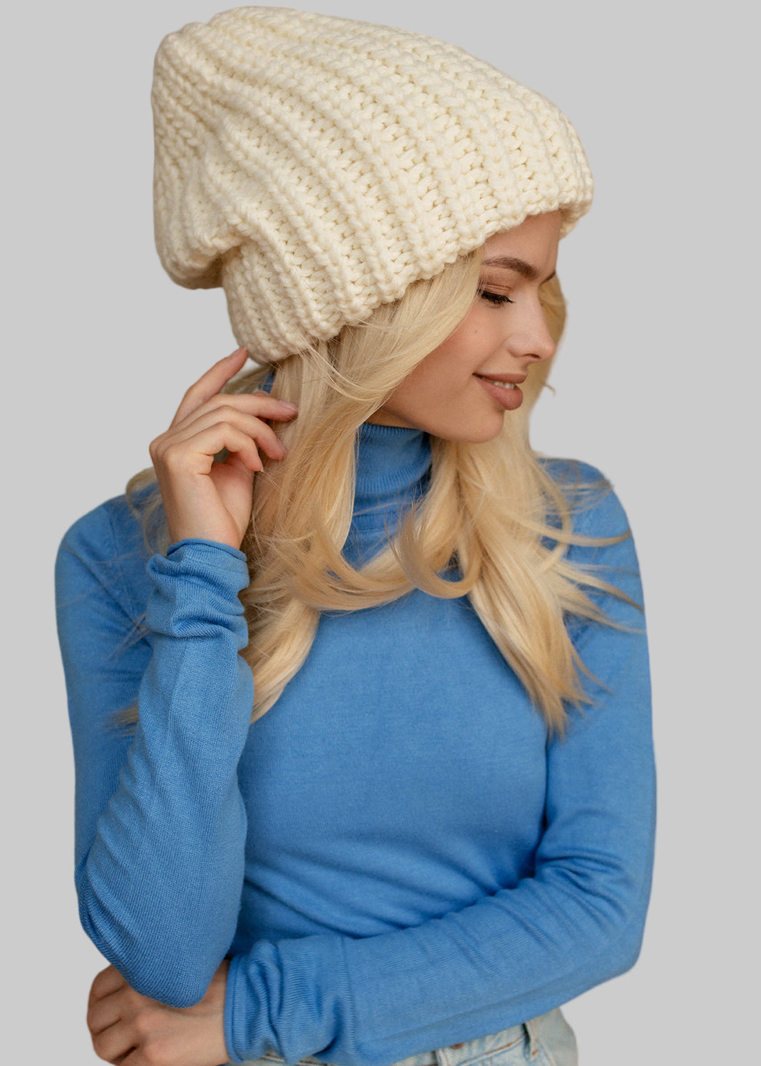 Woman wearing a cream beanie and blue sweater indoors